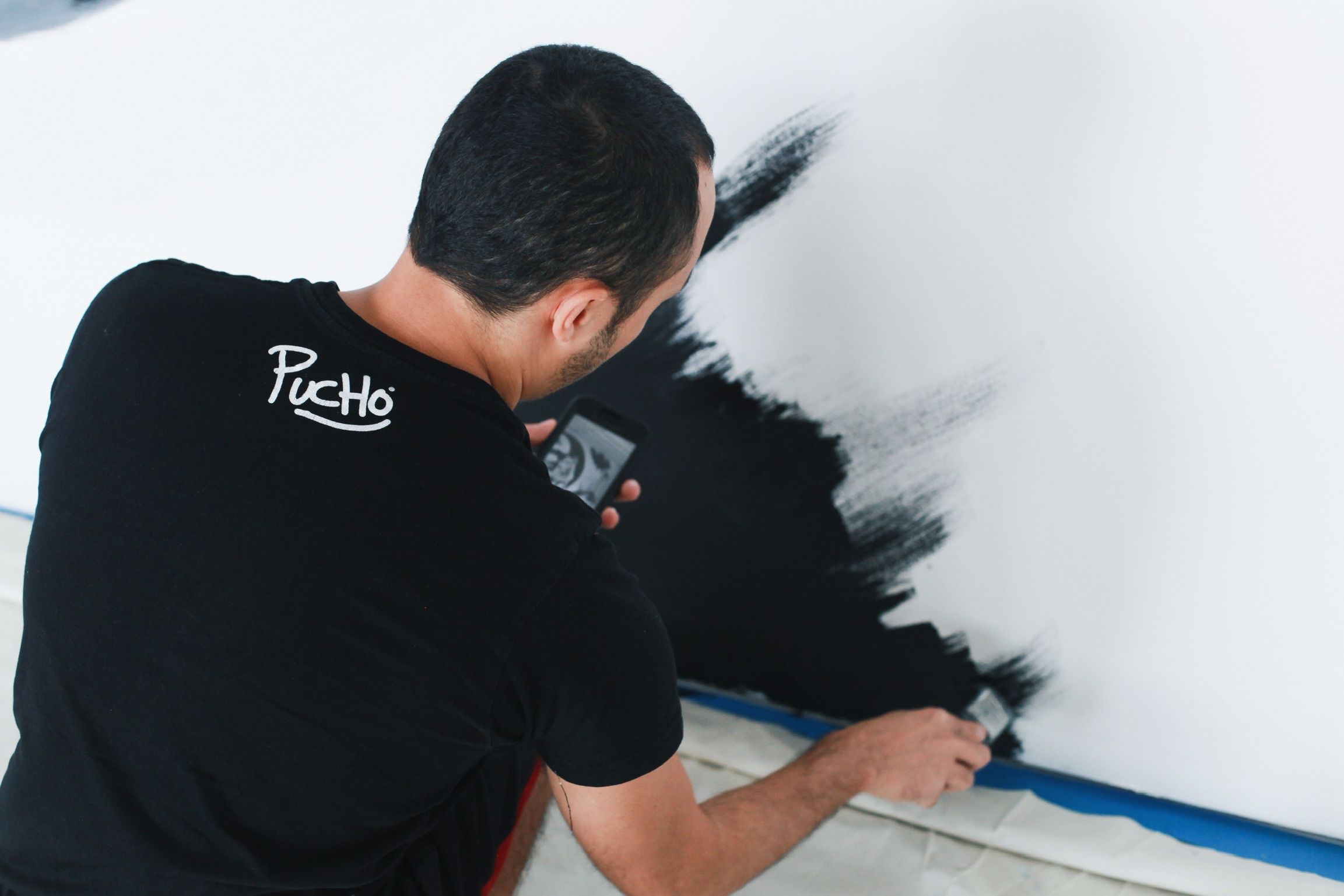 The artist brushing black paint onto a white wall