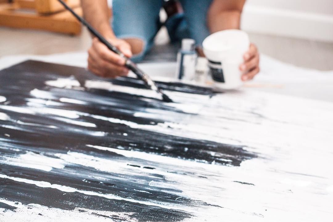 A brush dragging black paint across a white canvas