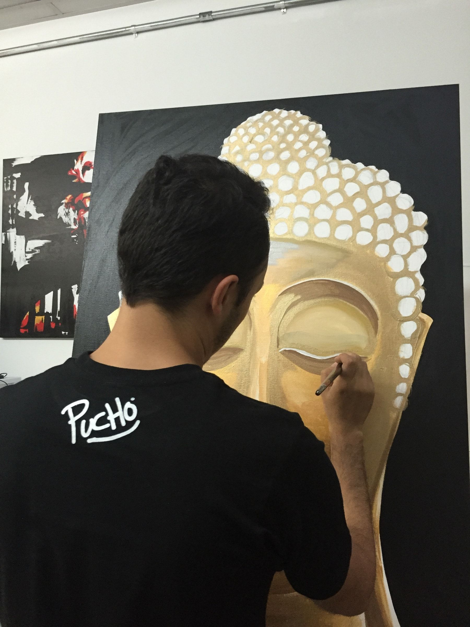 The artist painting a golden Buddha head on a large dark canvas