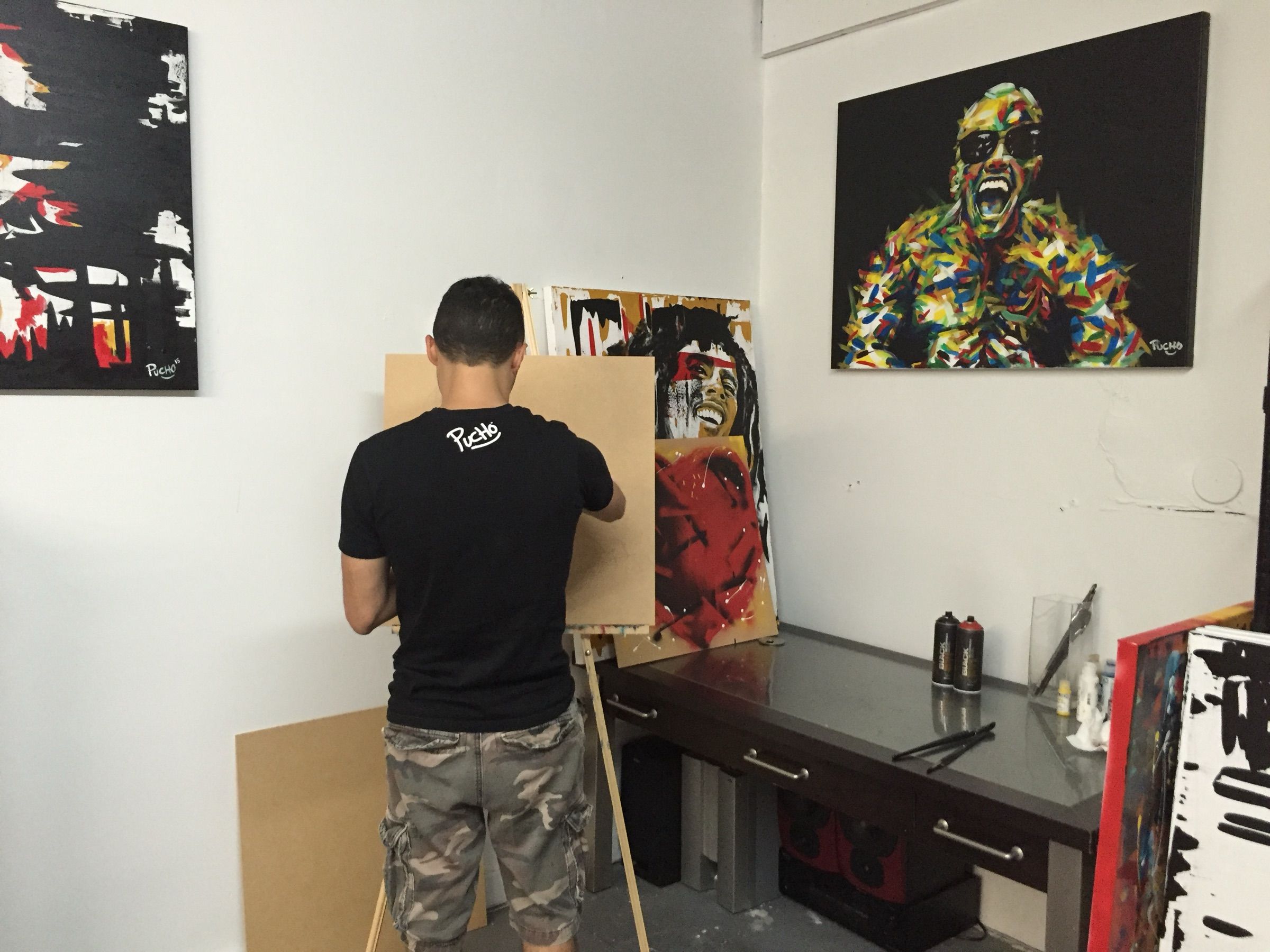 PUCHO at work in a white studio with finished paintings hanging on the walls
