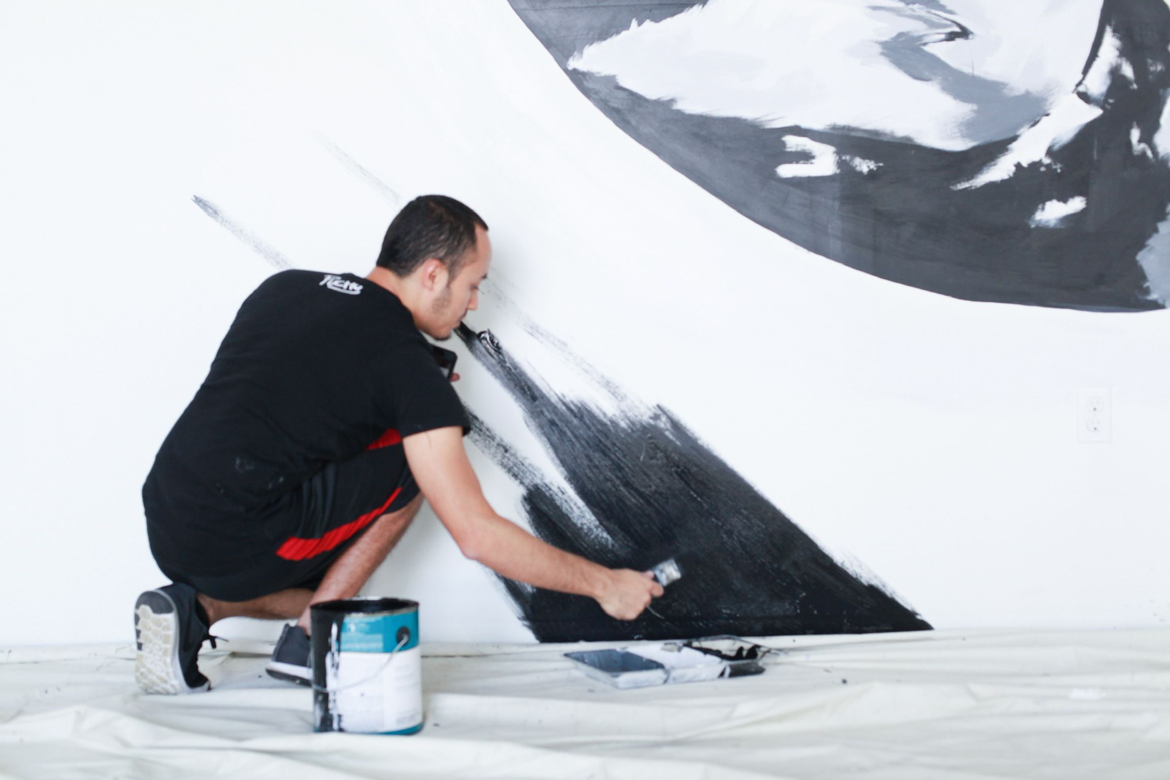 The artist painting the edge of a black geometric mural