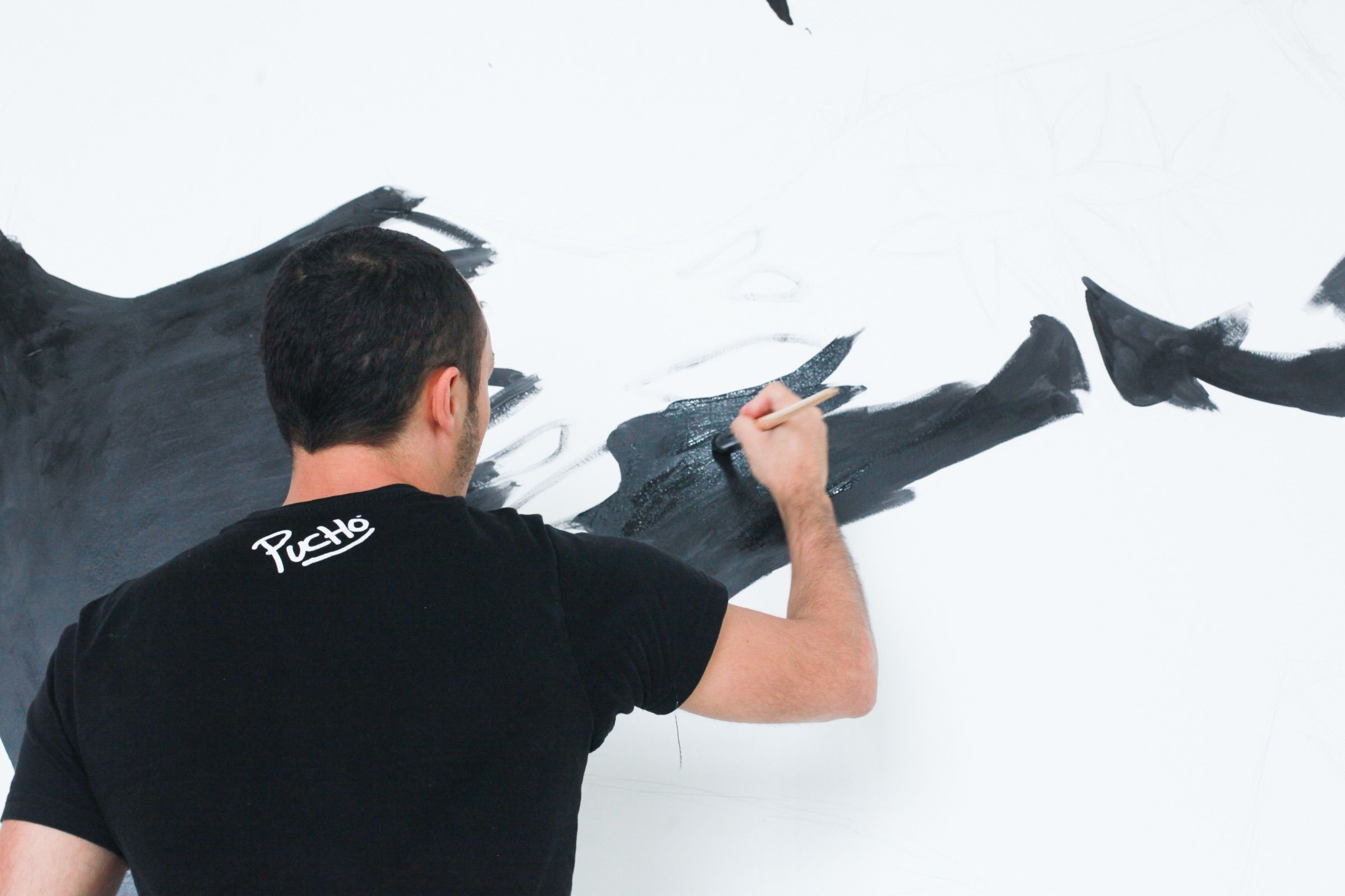 The artist painting sweeping black shapes on a white wall mural