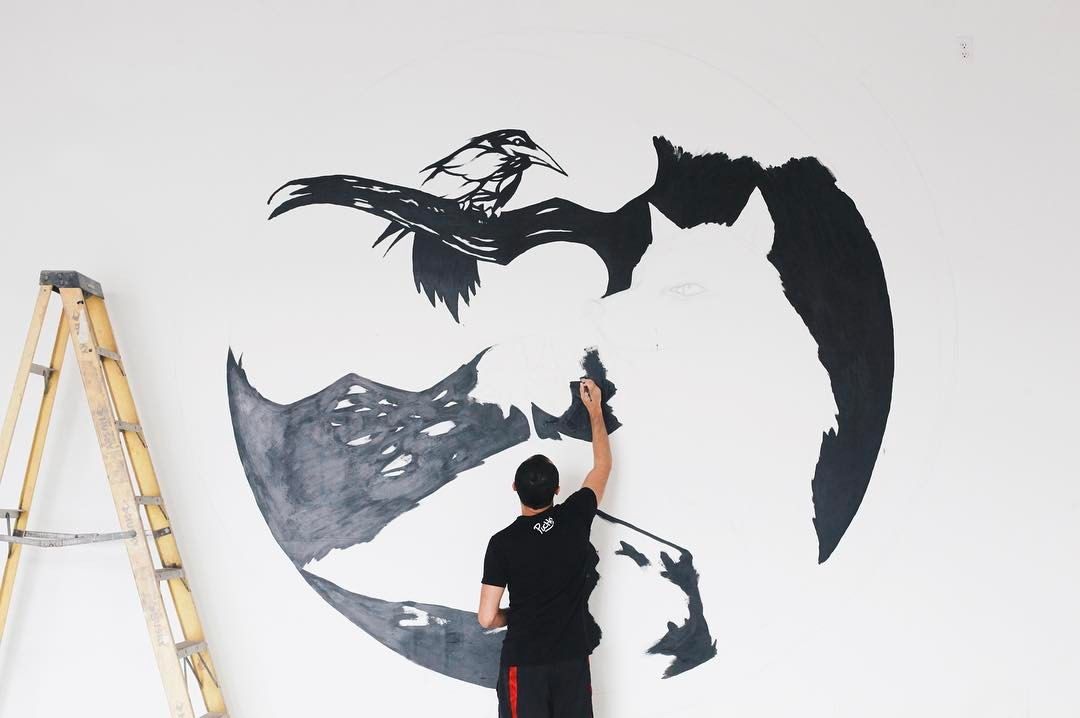 The artist painting a crescent moon mural with a raven in flight