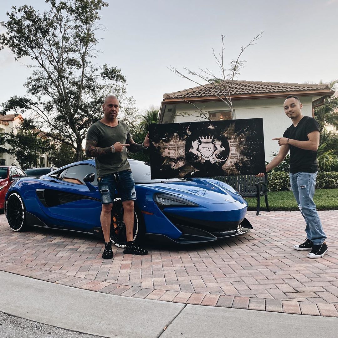 PUCHO and a collector presenting a painting beside a blue McLaren